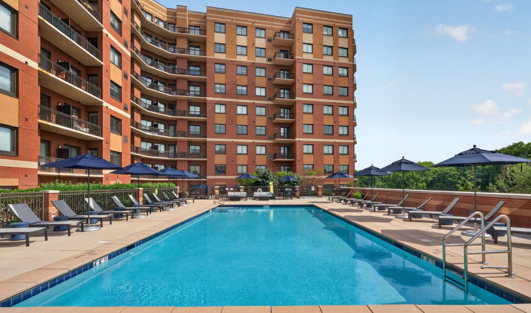 Pool deck with plenty of lounge chairs, umbrellas, and view of GW Bridge